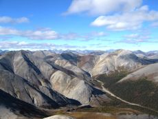 Plate tectonics is the means through which mountains are formed. Image shows rippled gray mountains, mostly treeless, beneath a cloud-studded blue sky. The Baird Mountains in Alaska&rsquo;s Kobuk Valley National Park formed when two tectonic plates along a convergent boundary collided, causing solid rock to buckle and fold.